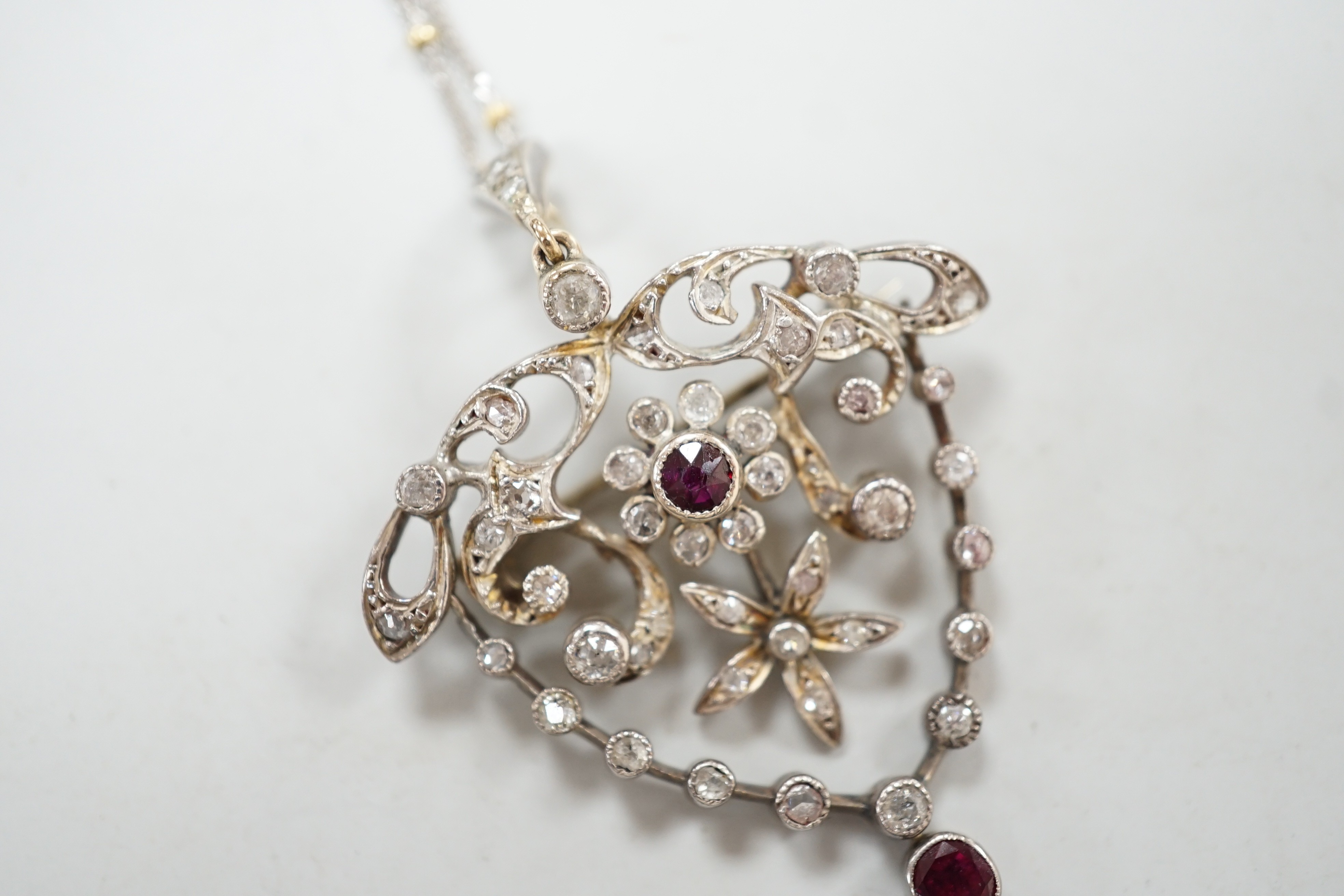 A yellow and white metal, ruby and diamond cluster set drop pendant brooch, 49mm, on an 18ct gold chain, 42cm, gross weight 11.5 grams.